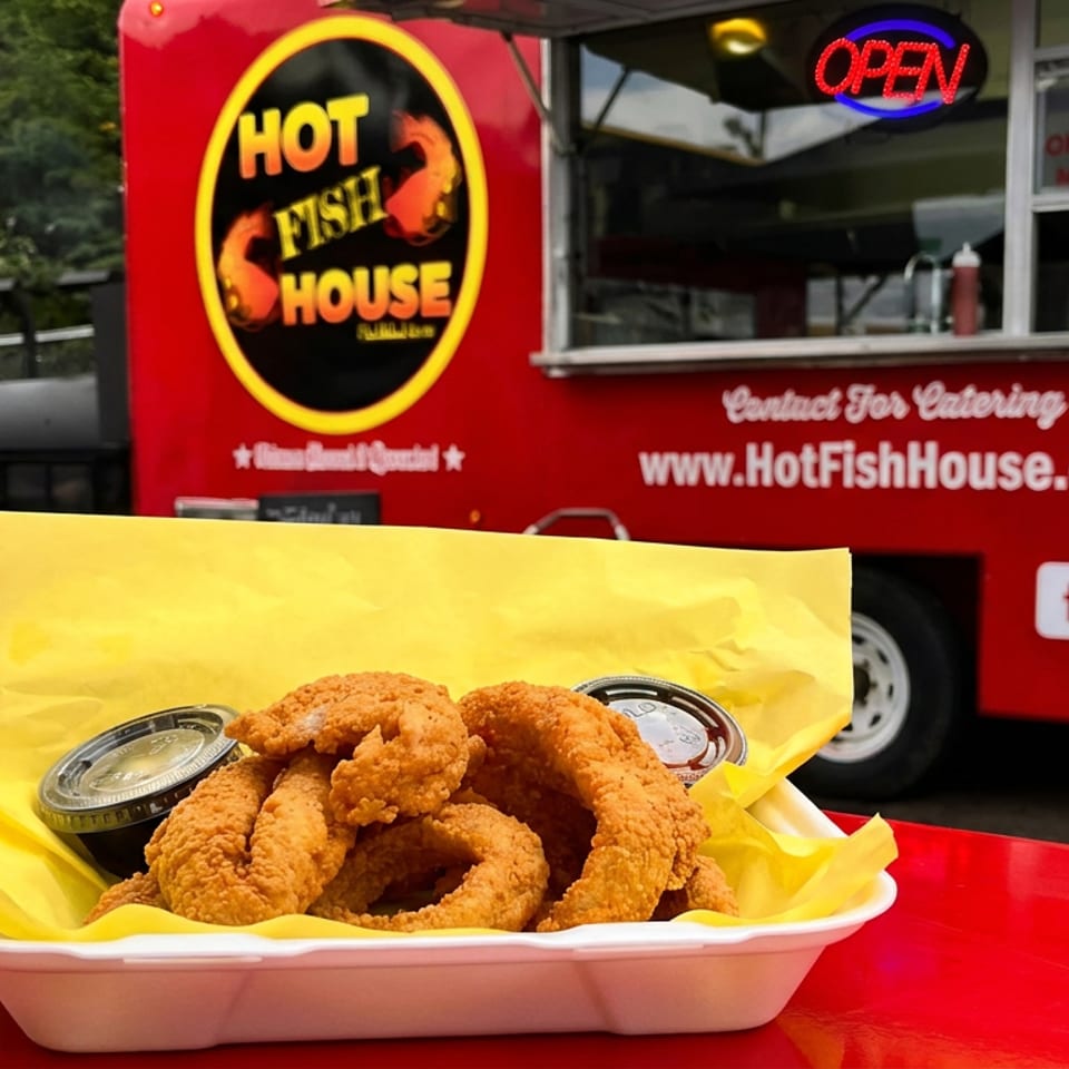 Crispy fried fish and onion rings with dipping sauces on a red table, in front of the Hot Fish House food truck.