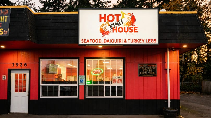 The red and black exterior of Hot Fish House, with a bright sign and neon "OPEN" sign in the window.